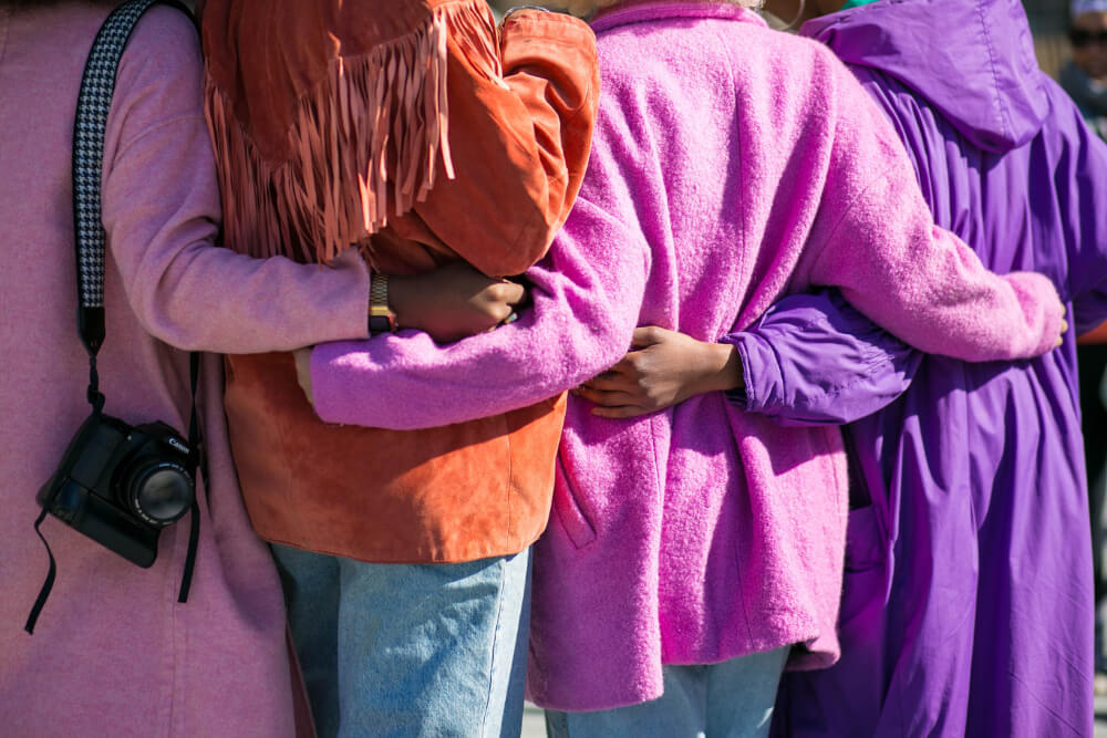 back of four women dressed in bright lilac, pink and orange coats as if celebrating International Women's Day with HIP